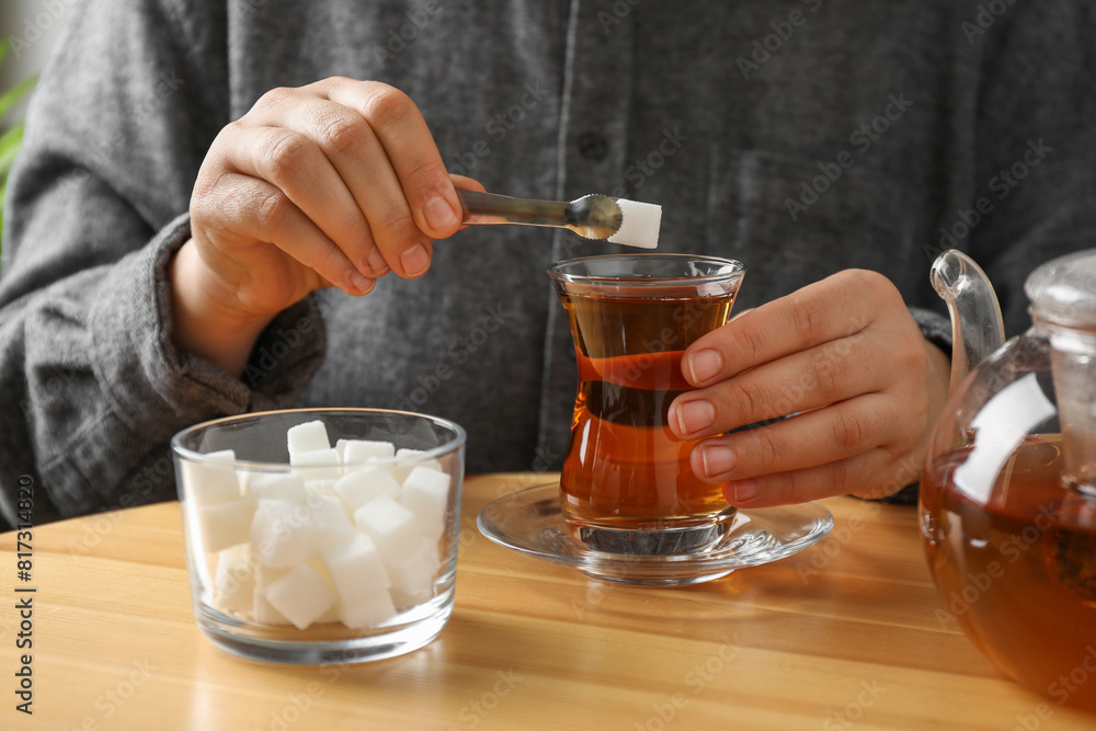 Woman adding sugar cube into aromatic tea at wooden table, closeup Woman adding sugar cube into aromatic tea at wooden table, closeup