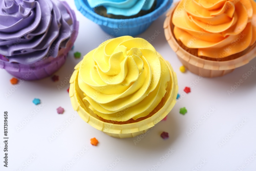Many tasty cupcakes with bright cream and sprinkles on white background, above view