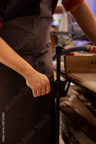Artisan using bench vise to hold lumber block, starting designing wood art in studio, close up shot. Woodworking specialist in carpentry shop using sash clamp to secure piece of wood tightly