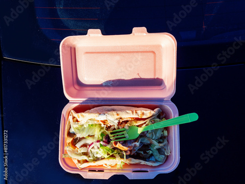 Chicken kebab wrap meal in a plastic pink container on blue car trunk. Take away food with high calorie count. Eating out concept. Arabic style food. Popular snack.