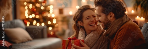 A happy couple shares a joyful moment exchanging Christmas presents against a backdrop of festive lights and decorations