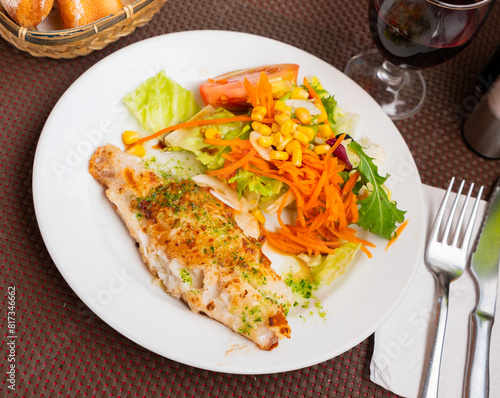 Appetizing deep fried fish fillet, chopped parsley and garlic in olive oil served with fresh vegetable salad on plate. photo