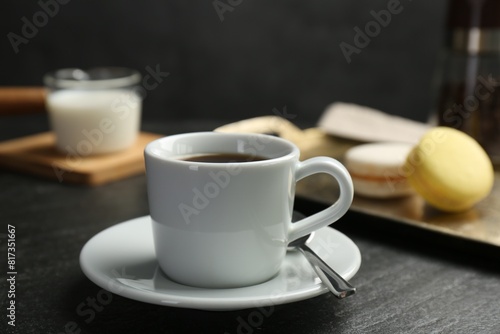 Hot coffee in cup, saucer and spoon on dark textured table, closeup