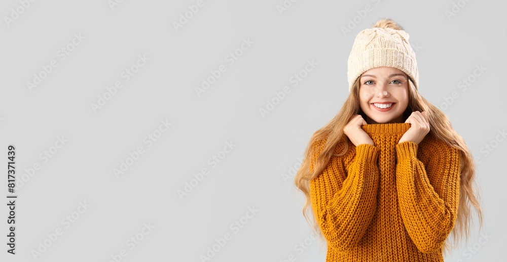 Happy young woman in warm sweater on grey background with space for text