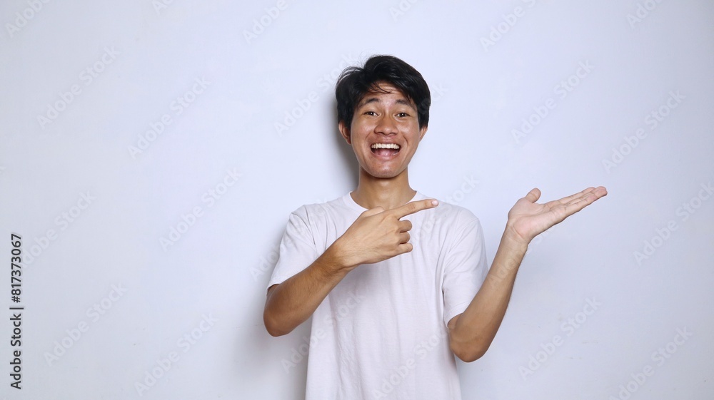 Excited young Asian man in white shirt with funny expression gesture pointing to open palm Excited young Asian man in white shirt with funny expression gesture pointing to open palm