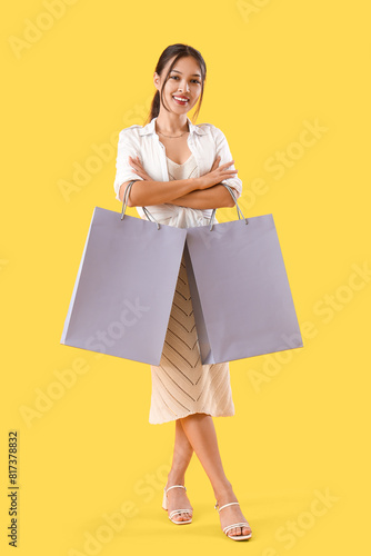 Young Asian seller with shopping bags on yellow background