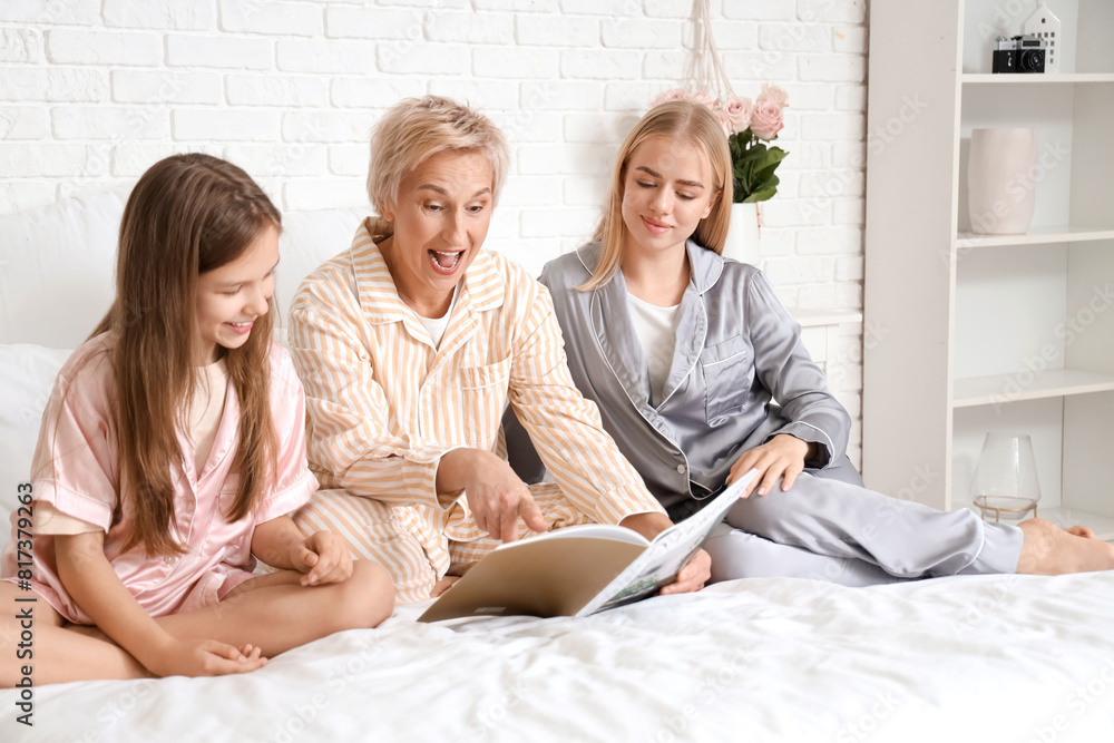 Little girl with her mom and grandmother reading magazine in bedroom Little girl with her mom and grandmother reading magazine in bedroom