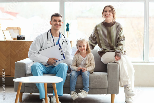 Male pediatrician, little girl and her mother sitting on sofa at home © Pixel-Shot