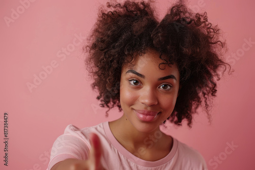 Photo of a happy black woman with afro hair wearing a casual t-shirt pointing his index finger at the camera on a pink background © boxstock production