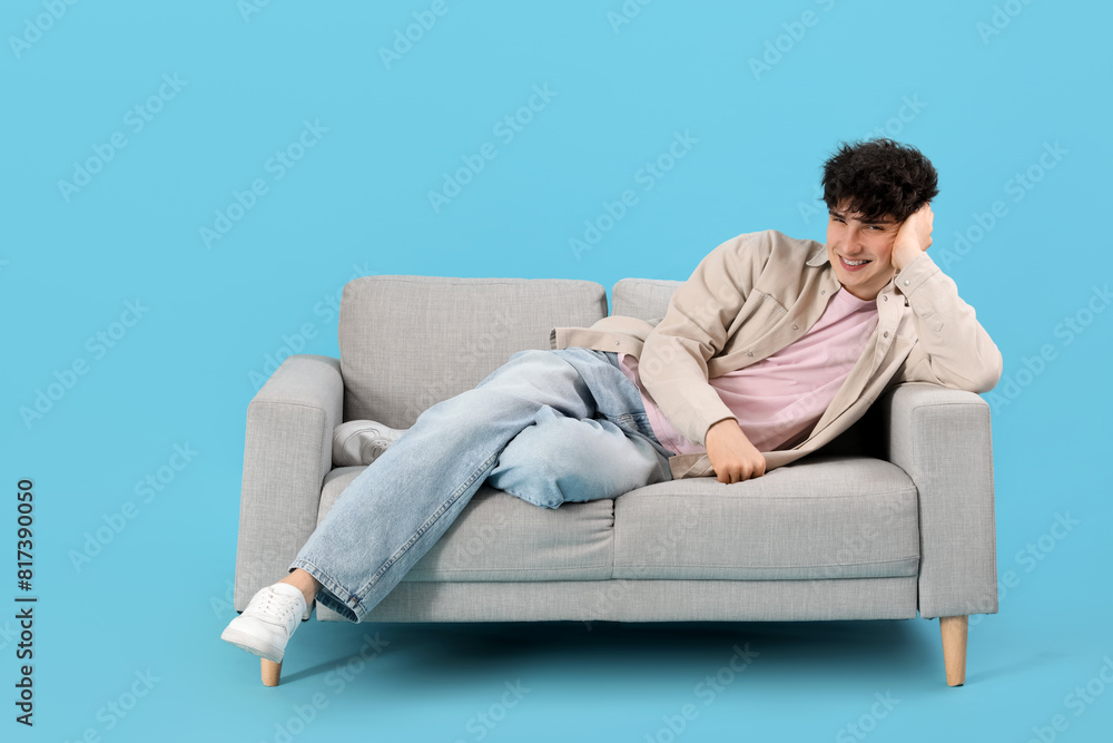 Young man resting on sofa on blue background