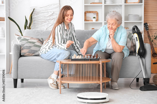 Senior woman and her granddaughter playing chess with robot vacuum cleaner at home