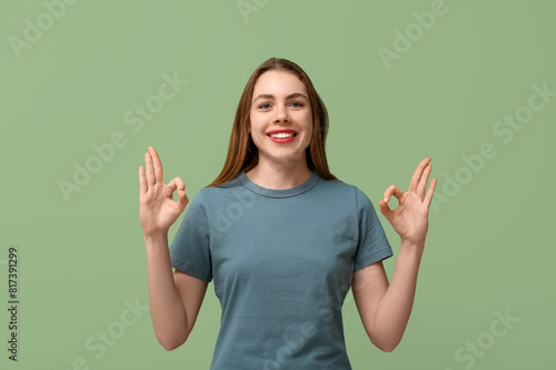 Young deaf mute woman using sign language on green background
