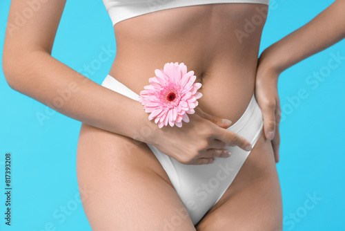 Beautiful young woman in panties with gerbera flower on blue background, closeup