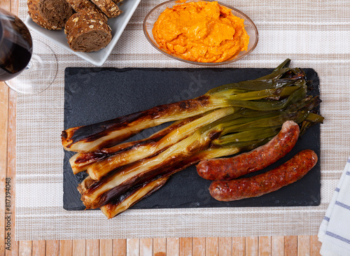 Traditional Catalan calcotada meal. Calcots roasted over open fire on slate serving board with spicy salvitxada sauce, multigrain bread and grilled botifarra pork sausages photo