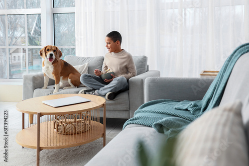Billede på lærred Little African-American boy with cute beagle dog eating cereal rings at home
