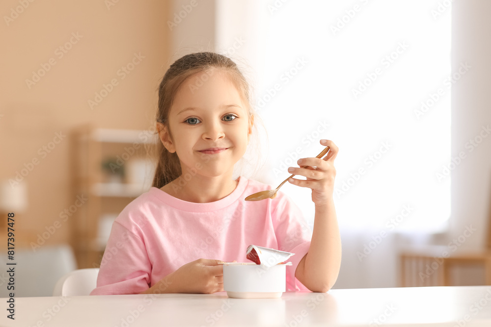 Cute little girl sitting by table and eating yogurt at home Cute little girl sitting by table and eating yogurt at home