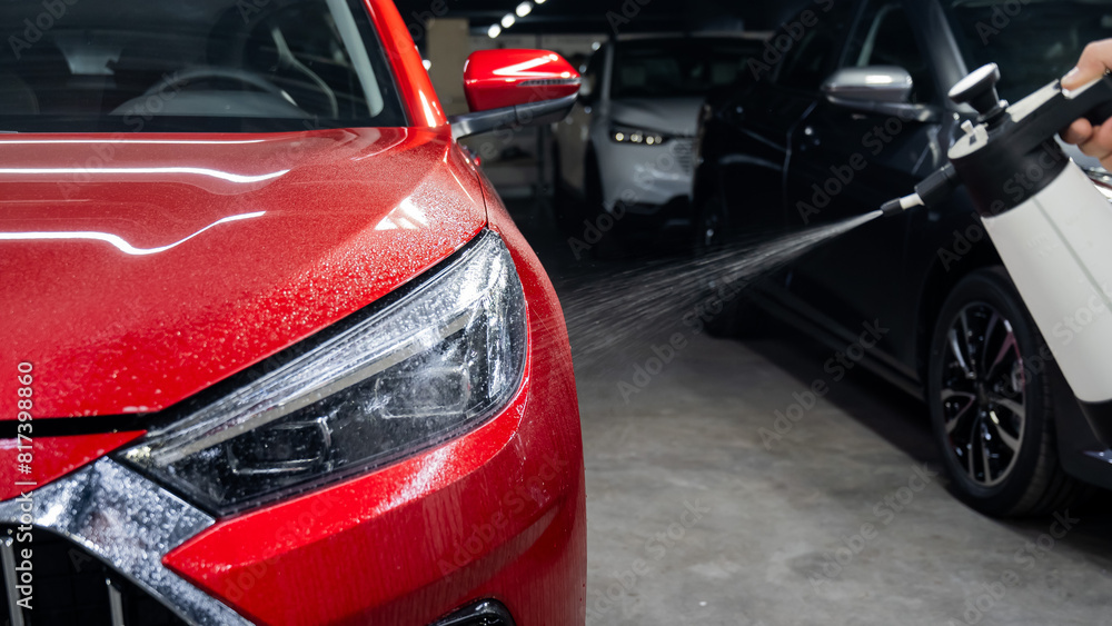 A man washes the headlights of a red car with a spray. 