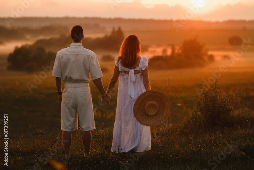 A couple in love in white clothes in a field at a red sunset