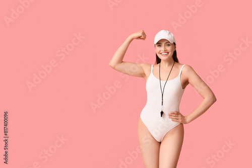 Female lifeguard with whistle showing muscles on pink background