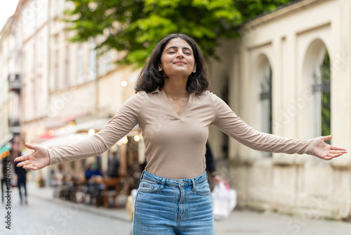 Indian young woman taking a deep breath of fresh air, relaxing, taking a break, resting, meditating, calm down outdoors. Hispanic girl enjoying happy day walking on urban city street. Town lifestyles