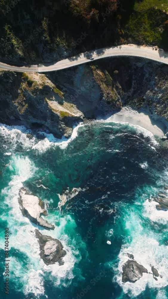 Vertical Screen: Aerial top down 4k view of travelers cars driving on ocean coastal road in green mountains on sunny summer day. Cinematic drone shot flying over cinematic highway road on rocky ocean Vertical Screen: Aerial top down 4k view of travelers cars driving on ocean coastal road in green mountains on sunny summer day. Cinematic drone shot flying over cinematic highway road on rocky ocean