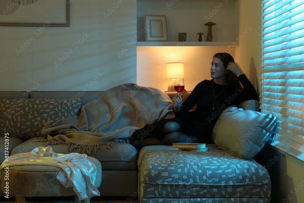 Woman with glass of wine resting on couch in room at night Woman with glass of wine resting on couch in room at night