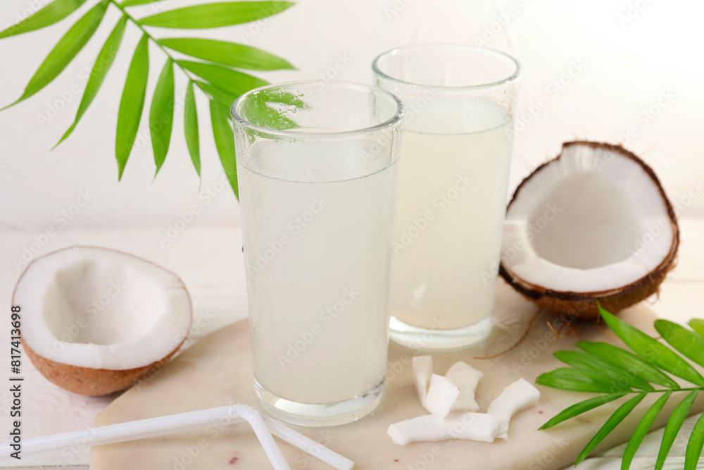 Glasses of coconut water, palm leaves and nuts on white table