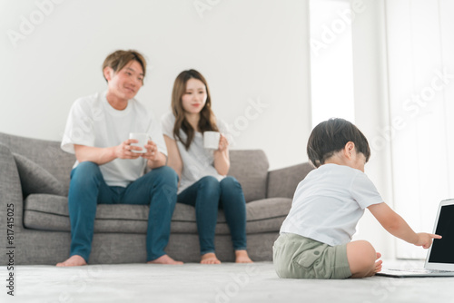 家のリビングでパソコンを使う子供と日本人夫婦（知育・家族） 