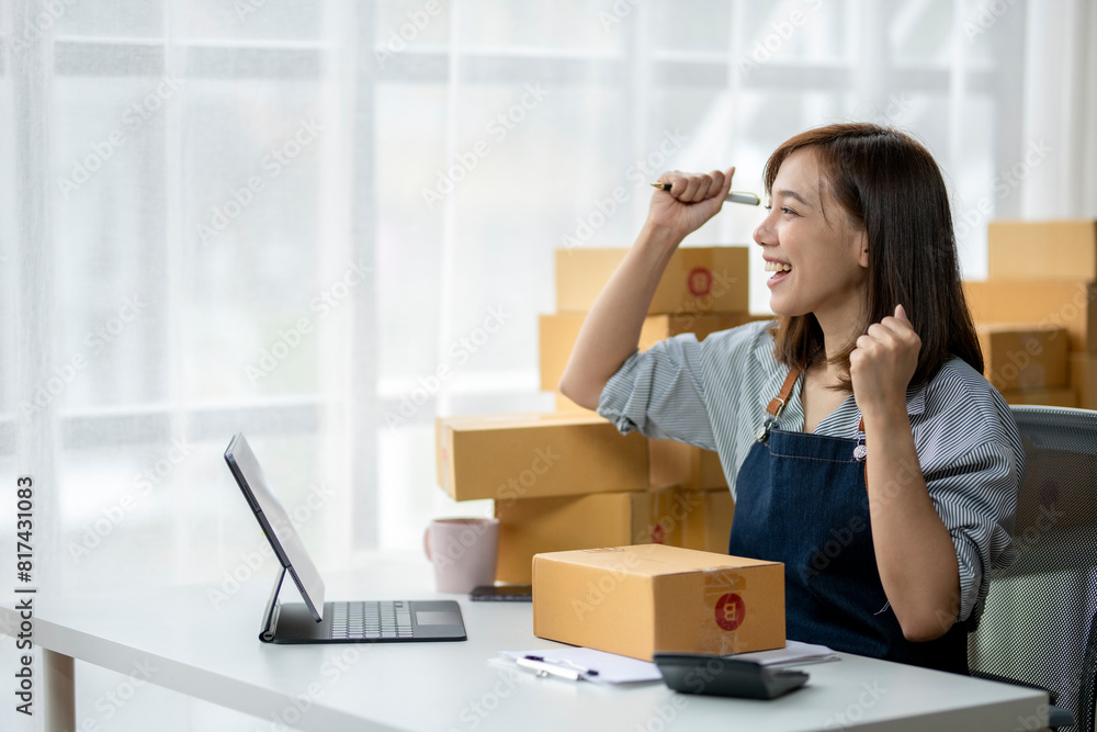 A woman is sitting at a desk with a laptop and a stack of boxes in front of her