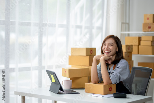A woman is sitting at a desk with a laptop and a stack of boxes in front of her