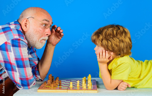 Grandson playing chess with grandpa. Games and activities for children. Grandfather teaching grandchild play chess. Board game. Checkmate. Little boy learning to play chess. Family relationship.