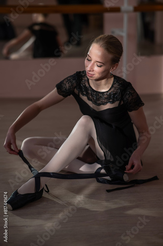 Woman sitting on the floor and tying ribbons on her pointe shoes. Vertical photo. 