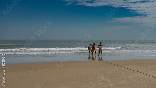 A team of people pulls a fishing net out of the ocean. The men are holding onto the rope. The waves are foaming on the beach. Reflection on the wet smooth sand. Madagascar. Morondava. 