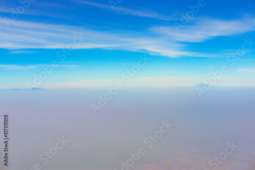 view of the bright blue sky and mountains on the island of Java from the plane window, blue sky with clouds, See Through Plane Window With Blue Sky And Clouds Outside, travel trip over Java island © Fani