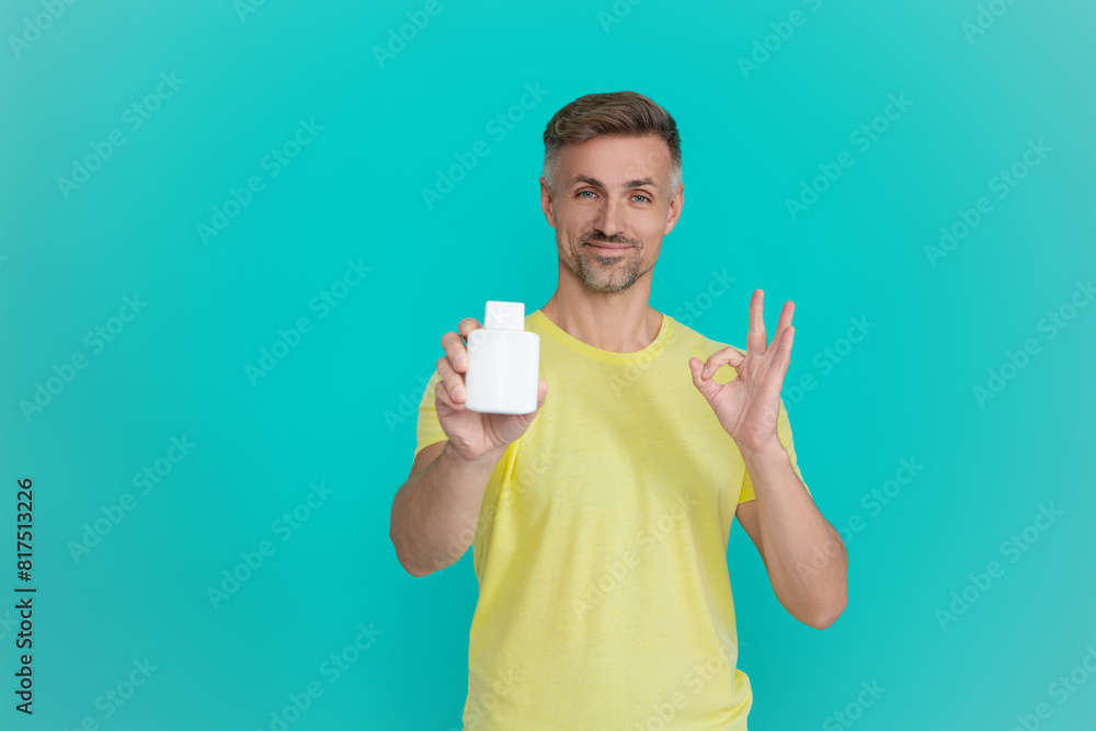 Man hold food supplement isolated on blue. Man with pill or vitamin. Presenting energy remedy. Multivitamins and vitamin. Daily supplement. Offer medication. Medication to relieve pain. Ok Man hold food supplement isolated on blue. Man with pill or vitamin. Presenting energy remedy. Multivitamins and vitamin. Daily supplement. Offer medication. Medication to relieve pain. Ok