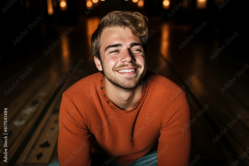 smiling young man sitting on hardwood floor with eyes closed smiling young man sitting on hardwood floor with eyes closed