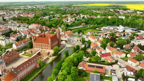 Castle with Tower, River and canola field in small polish town of Lidzbark Warminski. Sunset time lighting on old town in Poland. Aerial wide shot. photo