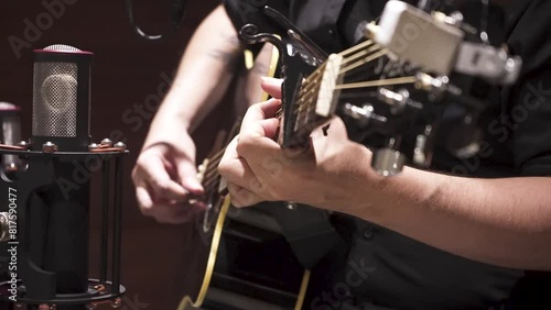 Guitarrista tocando guitarra acústica con transporte, en estudio de grabación con una camisa negra. Footage de música, musical, grabación en estudio, producción musical. photo