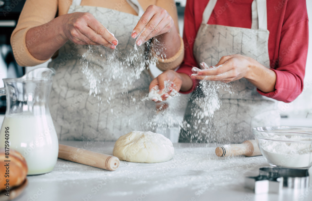 Close up image of hands of mother and daughter spreading wheat flour on the dough and preparing pastries in the kitchen at home Close up image of hands of mother and daughter spreading wheat flour on the dough and preparing pastries in the kitchen at home