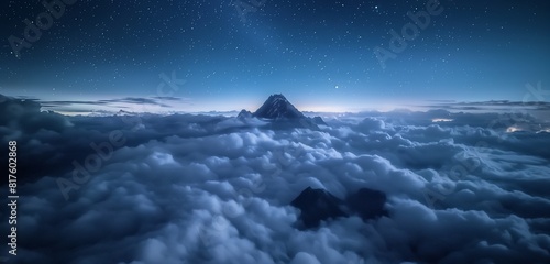 The peak of a mountain visible above dense  low-lying night clouds  illuminated from above by the moon and stars. 32k  full ultra HD  high resolution