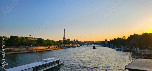 View of the River Seine at sunset on a summer day with the Eiffel Tower in the distance, clear blue sky, French and European flags visible and boats