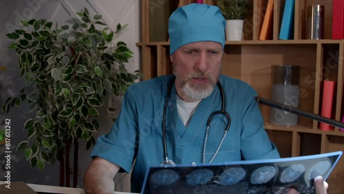 Close-up of middle aged male general practitioner in uniform examining MRI brain scan of sick patient , being puzzled by checkup and pondering over treatment plan while working at medical office.