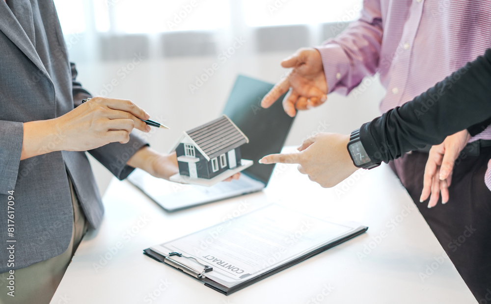 An official's hand points to a house model and explains details, contracts, and insurance to the couple who come to buy the house An official's hand points to a house model and explains details, contracts, and insurance to the couple who come to buy the house