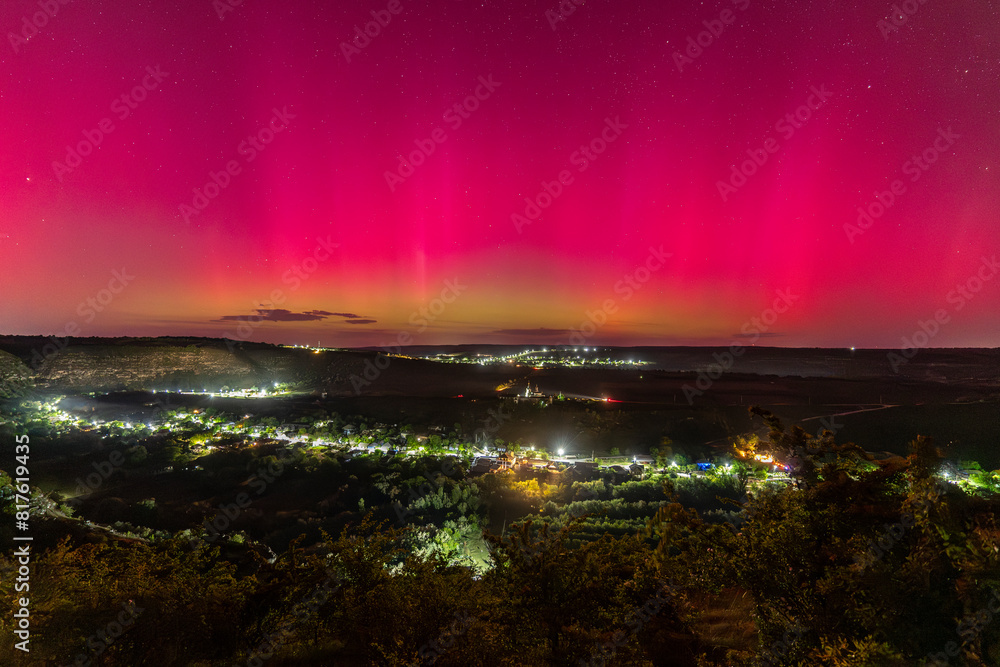 beautiful view on church on hill and village of butuceni in old orhei in moldova under bright pink purple green aurora borealis northern lights at night