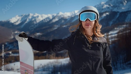 Woman snowboarder at snowy mountains. Happy woman snowboarder in costume and goggles with snowboard in hands at snowy mountains background. Having good time in holiday. Active extreme riding. photo