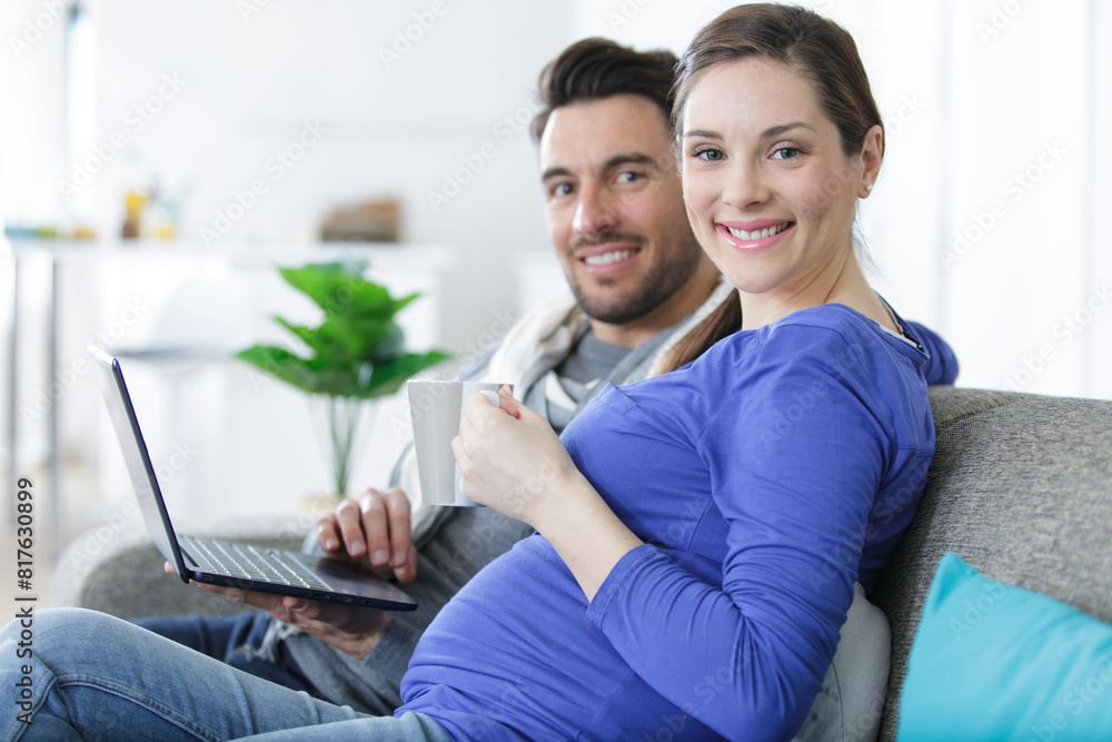 pregnant woman with husband using laptop while sitting at sofa pregnant woman with husband using laptop while sitting at sofa