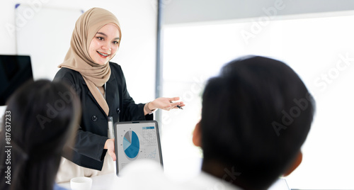 Young Asian Islamic businesswoman leading a discussion during a meeting with her colleagues. Group of diverse businesspeople working together in a modern workplace.