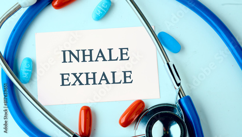 INHALE EXHALE written words on a white business card on a blue background with a stethoscope, pills in a composition in cold tones