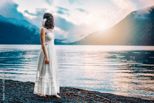 Teen girl with bow looking out at sunset over a lake and mountains photo