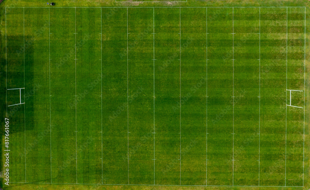 Straight down aerial drone photo of a man cutting the grass of a British rugby pitch in the summer time showing the mower going down the sports field